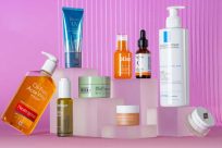 A variety of skincare products, including creams, serums, and lotions, are displayed on clear, staggered platforms against a pink background.
