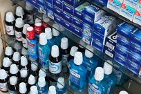 Shelves filled with various oral care products, including bottles of mouthwash in different colors and brands, and multiple boxes of toothpaste stacked neatly. The products have an organized and tidy arrangement.